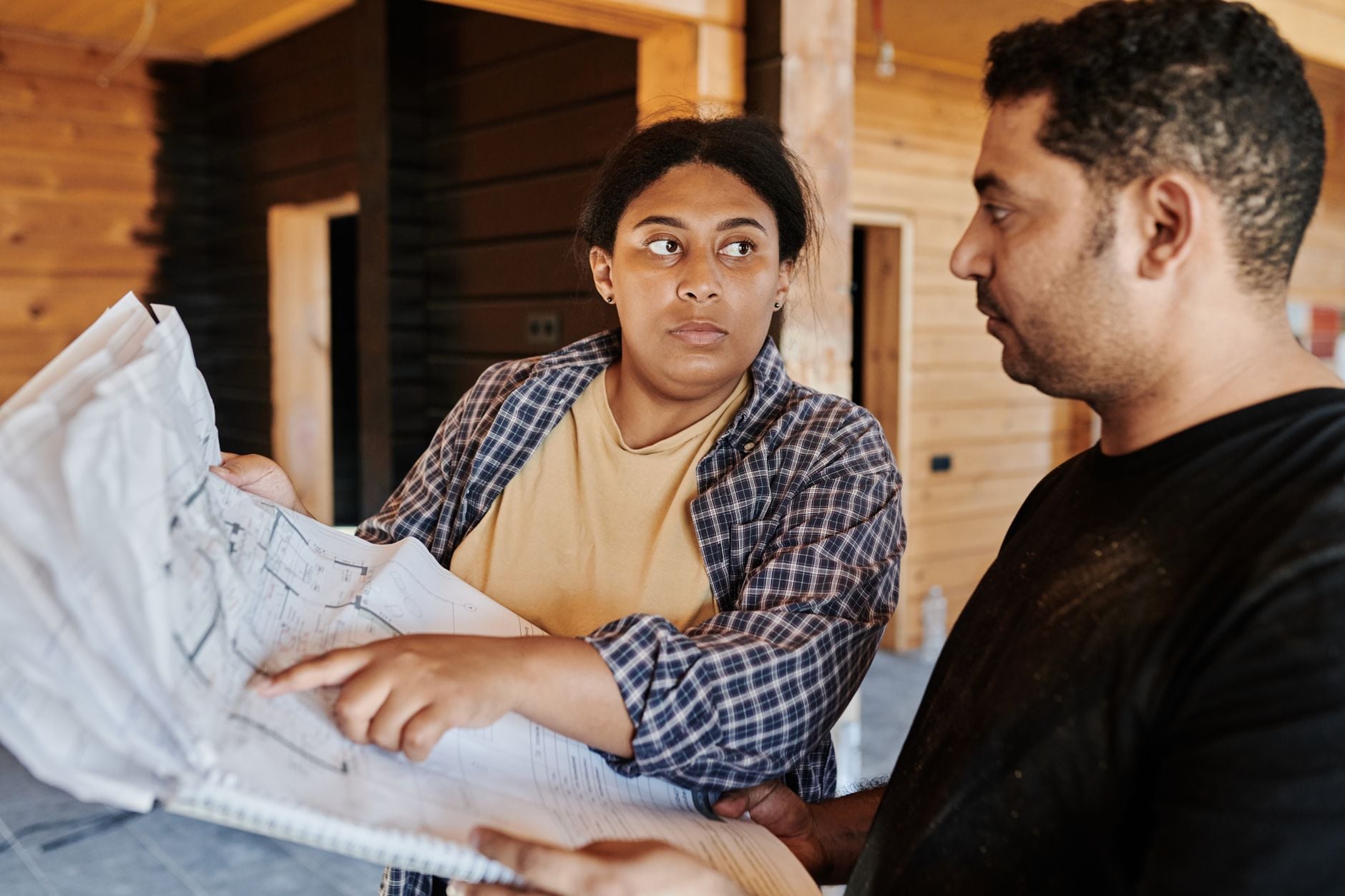 Two architects analyze blueprints in a wooden interior, focused on project planning and construction details.